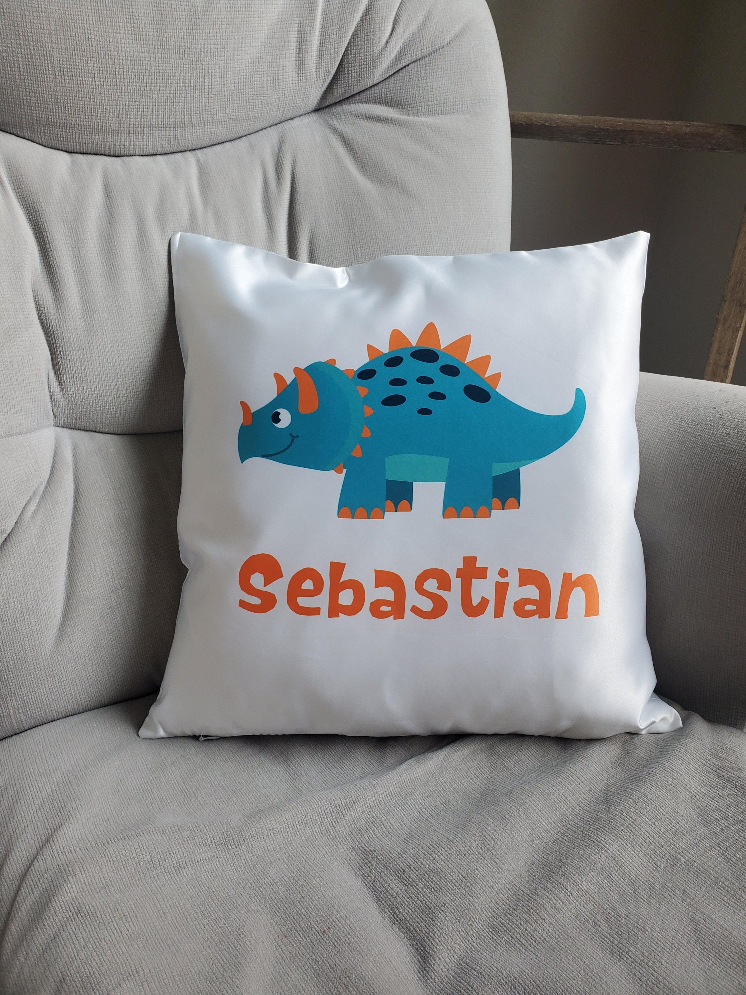 Gifts for Boys - Rejoice In Creation This image shows a pillow with the name Sebastian with a triceratops in orange and light blue cartoon style.